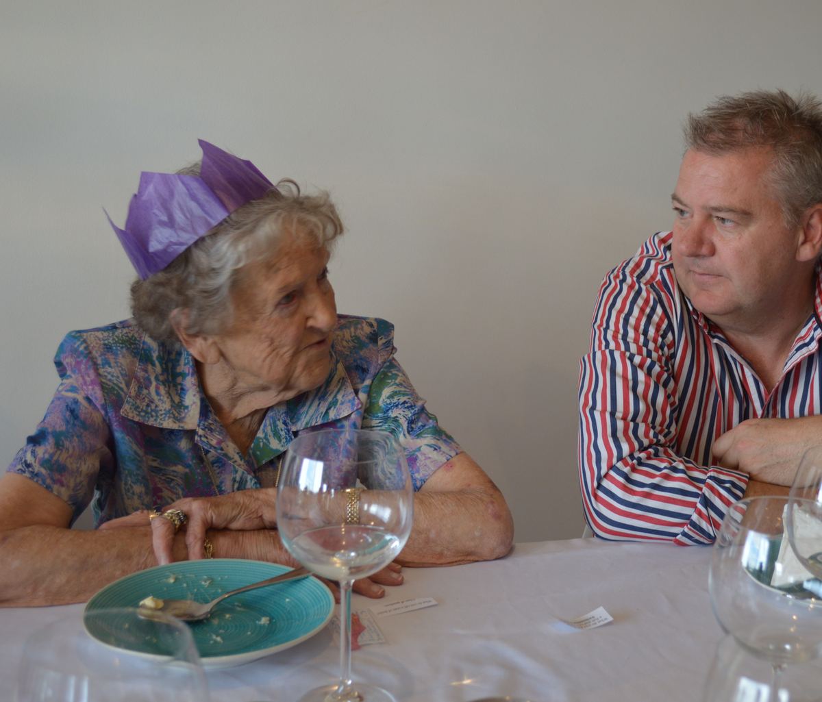 An older woman in a paper crown at a birthday lunch.