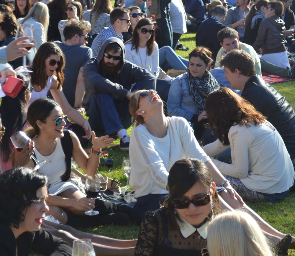 A crowd on the grass at an outdoor festival, one woman laughing.