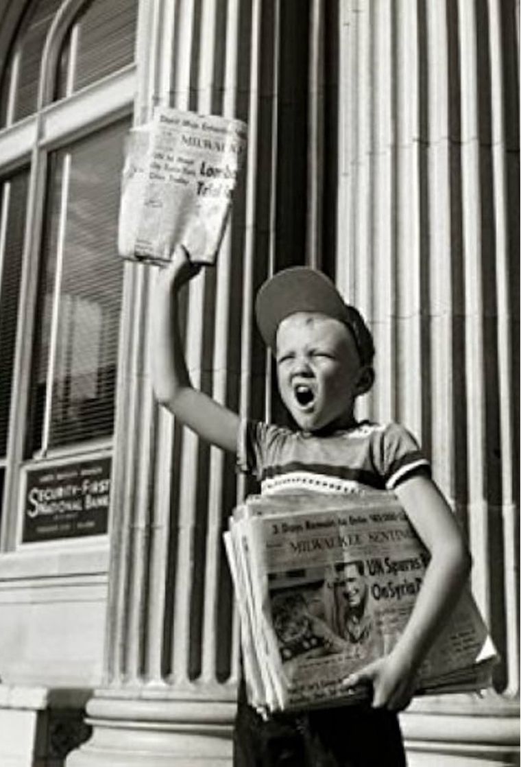 A newsboy holding up a paper and calling the headline.